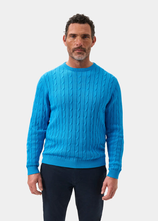 Man wears Honley Cotton Cashmere Cable Knit Crew Neck Jumper in Blue Lagoon, regular fit, with dark pants.