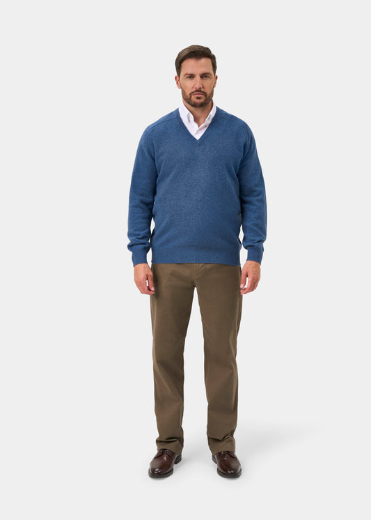 Man wears Hampshire Lambswool Vee Neck Jumper in Jeans, white shirt, khaki pants, brown shoes on white background.