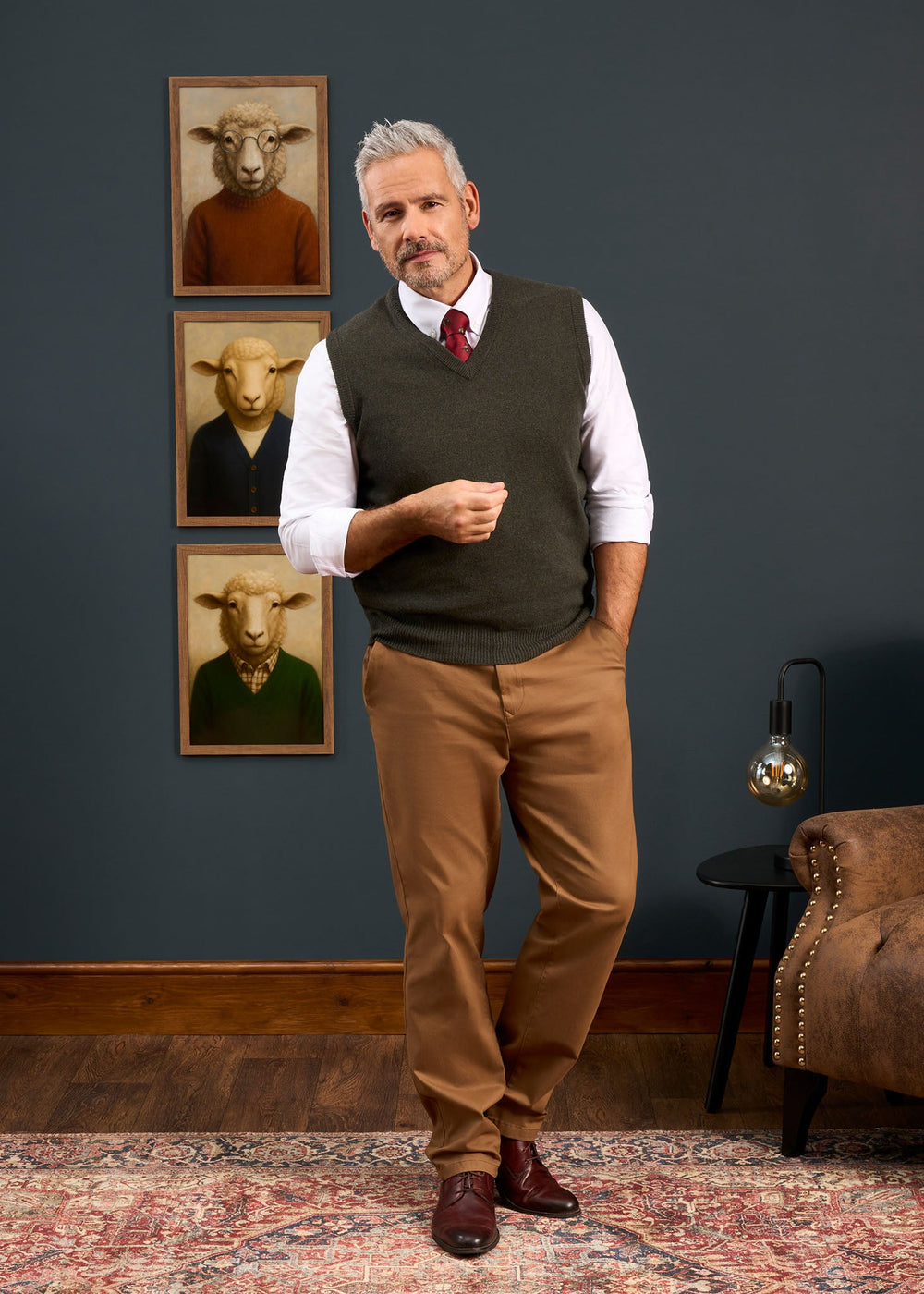 A man in a Norfolk Lambswool V-Neck Slipover In Seaweed over a white button-down shirt and brown trousers.