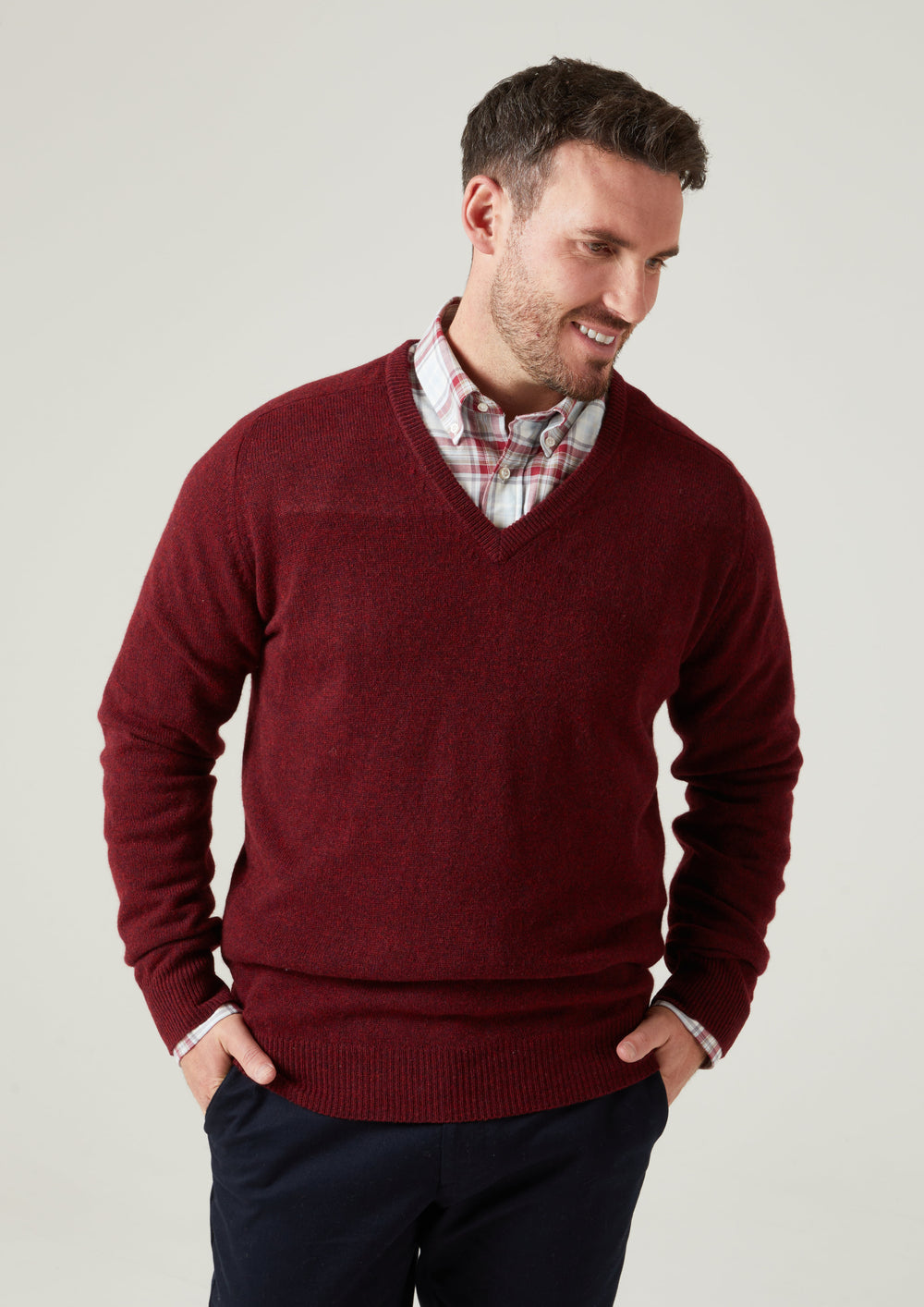Smiling man in Hampshire Lambswool Vee Neck Jumper in Red Velvet over plaid shirt, hands in pockets.