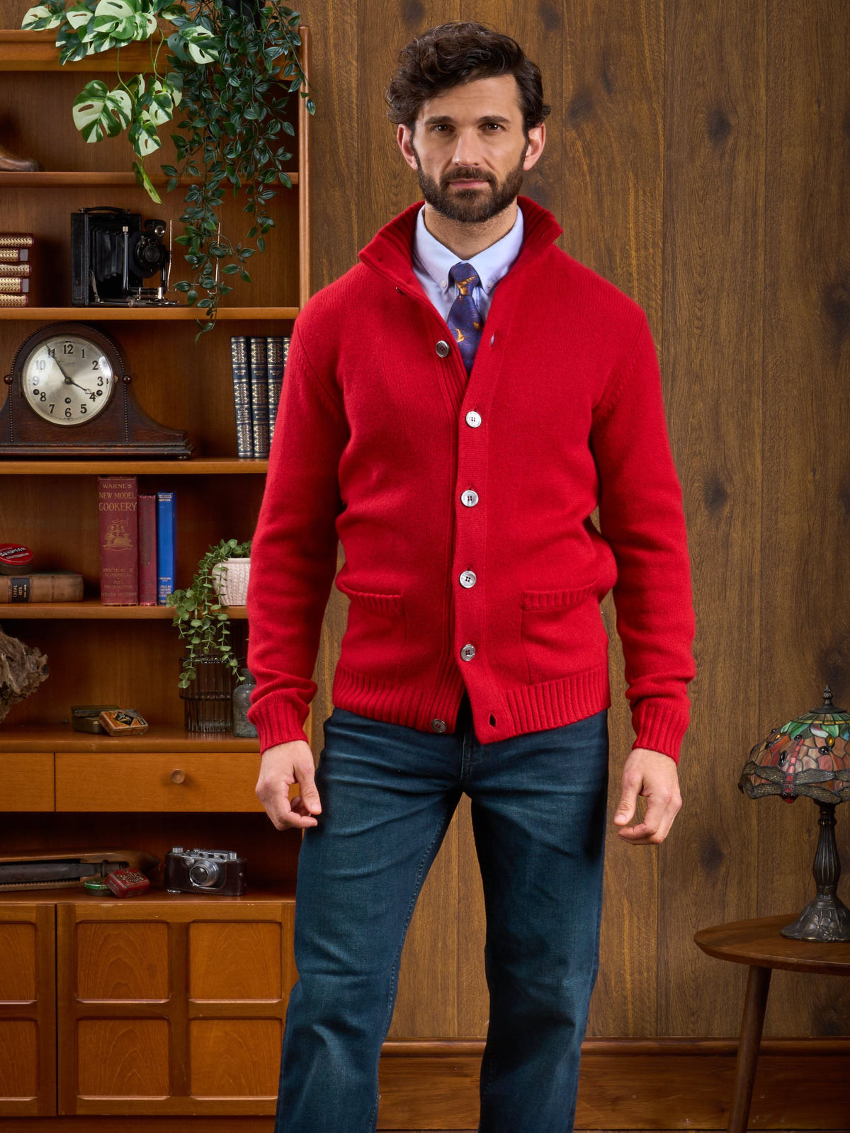 Man in a Landford Lambswool Mock Neck Jumper stands in a vintage room with wooden shelves and retro decor.