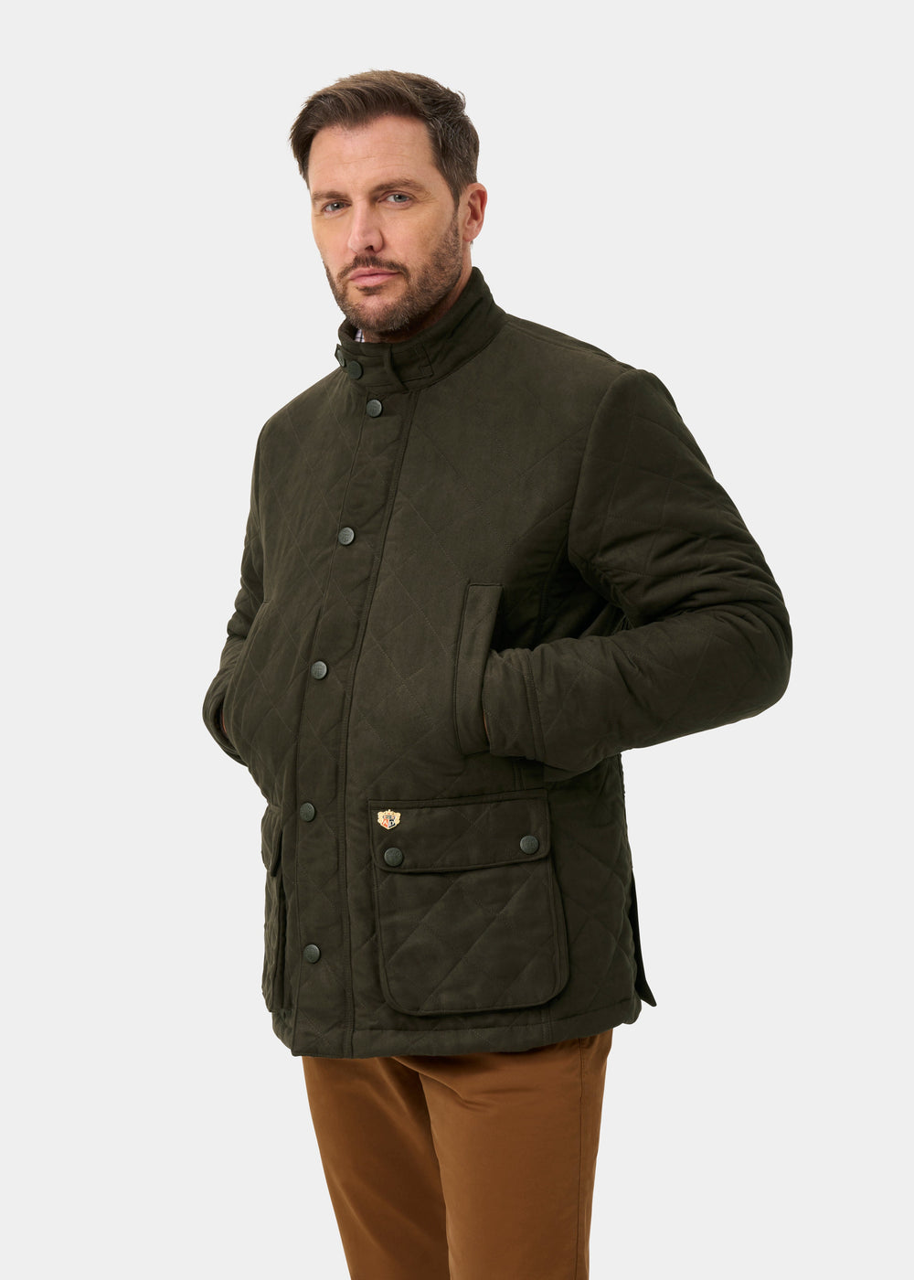 Man in Felwell Men’s Quilted Jacket in Olive, hands in pockets, against a plain light background.