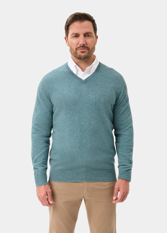 Man wears Haddington Caspian pure cashmere V-neck jumper over white shirt and tan pants, on a white background.