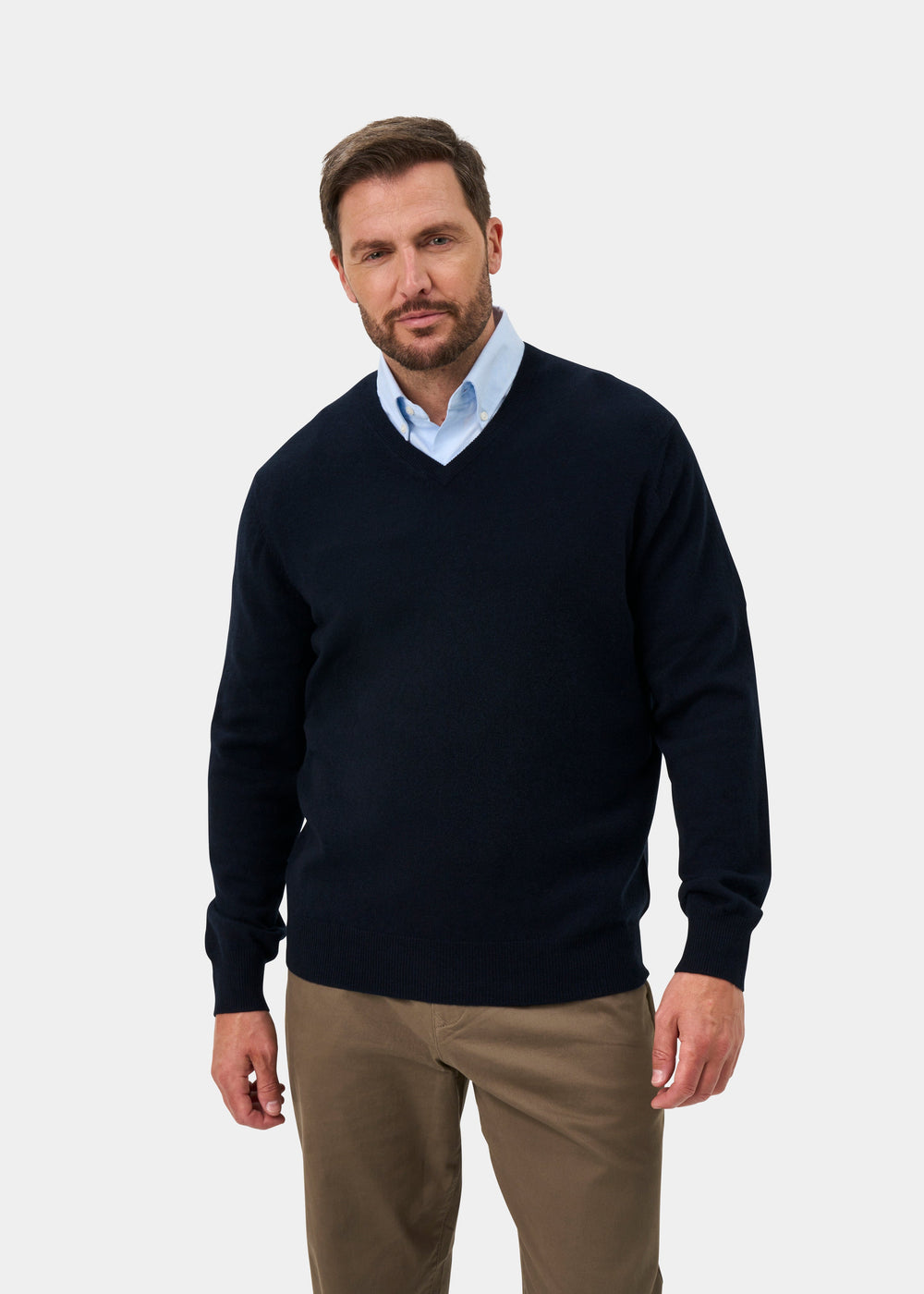 Man in Haddington Pure Cashmere V-Neck Jumper, dark navy, over light blue shirt and khakis, against plain background.