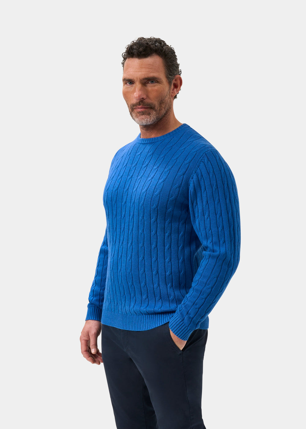Man with short curly hair in Honley Cotton Cashmere Cable Knit Crew Neck Jumper in Regatta, against a white background.