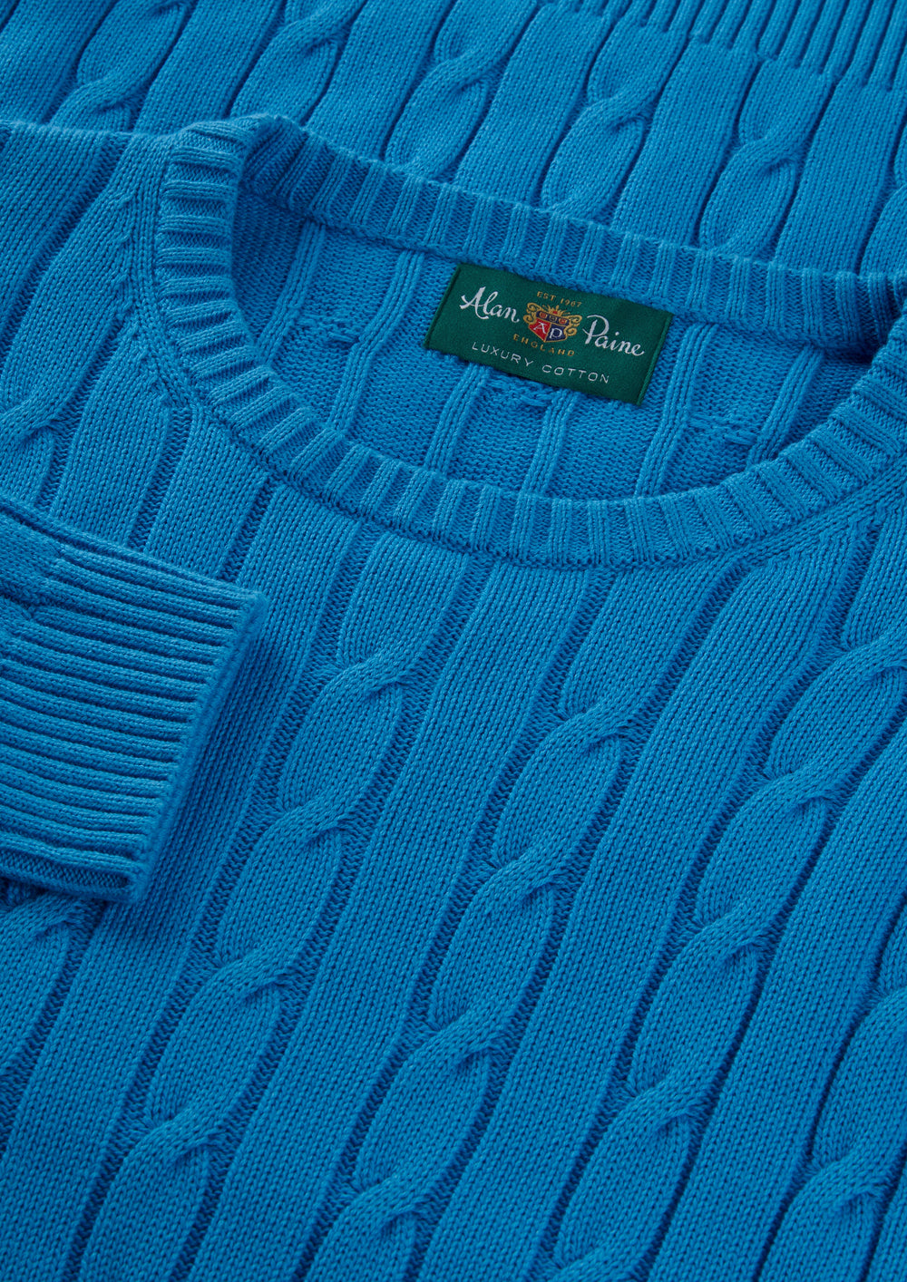 Close-up of Honley blue lagoon cable crew neck jumper; visible collar tag: Alan Paine Luxury Cotton Cashmere.