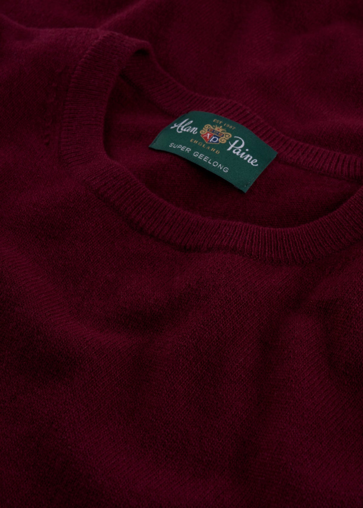 Close-up of a Brisbane Geelong Wool Crew Neck Jumper in Claret with green collar label.