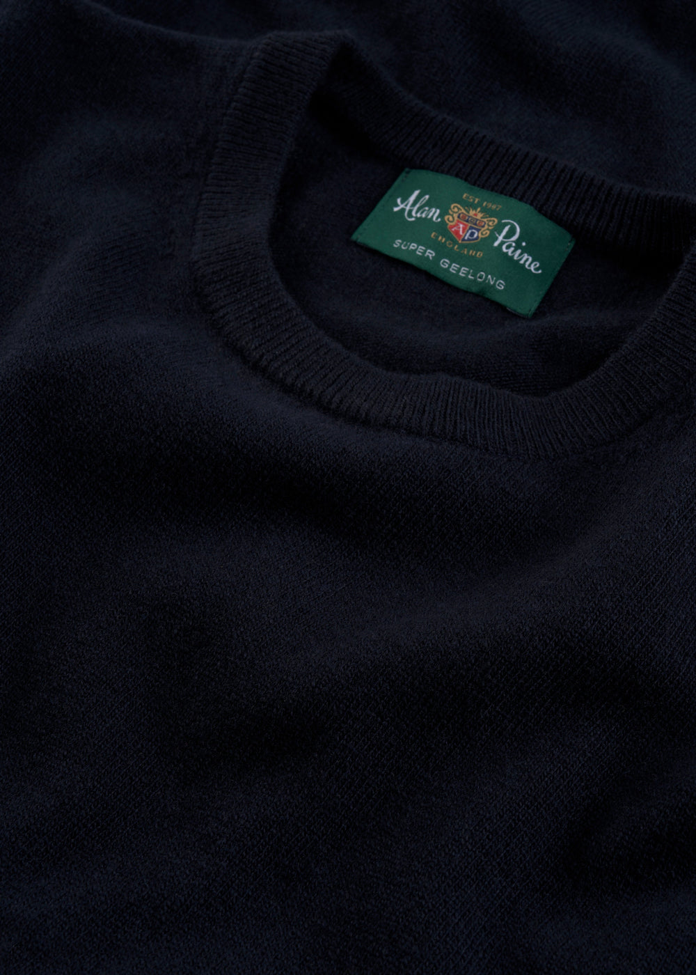 Close-up of a Brisbane Geelong Wool Crew Neck Jumper in Dark Navy - Regular Fit, featuring a green label.