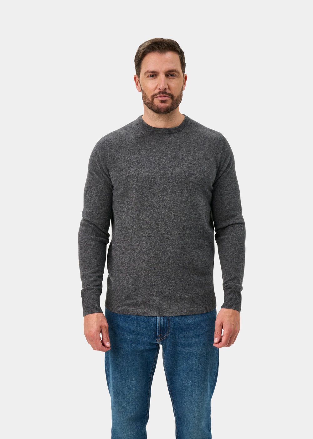 Man wears Brisbane Geelong Wool Crew Neck Jumper in Derby, regular fit, with blue jeans against a white background.