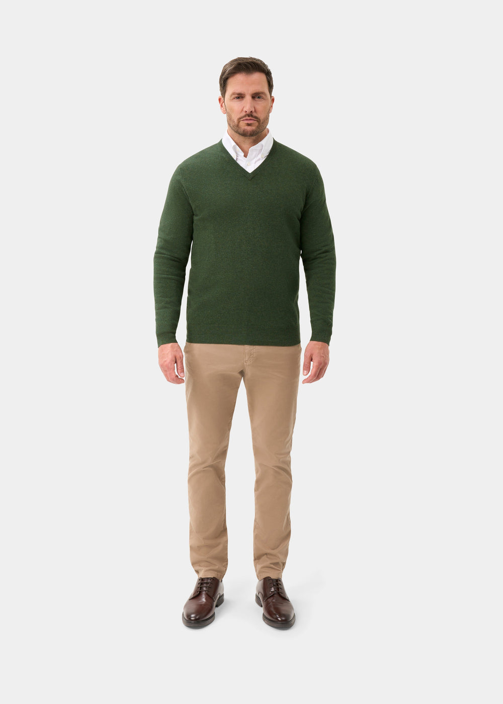 Man wears Albury Geelong Wool V-Neck Jumper in Rosemary, white shirt, khaki pants, and brown shoes on white background.