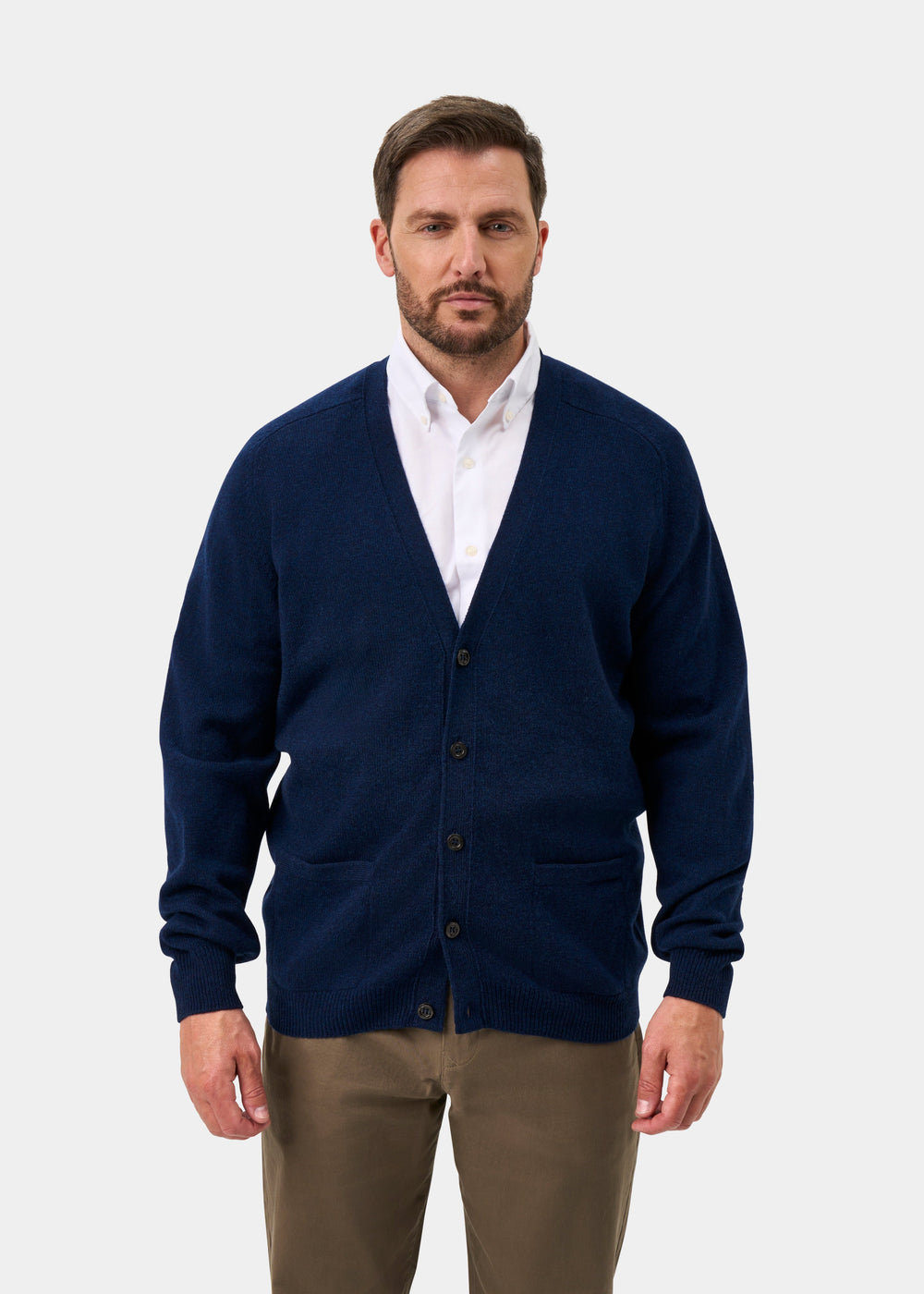 Man in Cornwall Lambswool V-Neck Cardigan in Indigo over a white shirt and brown pants, on a light background.