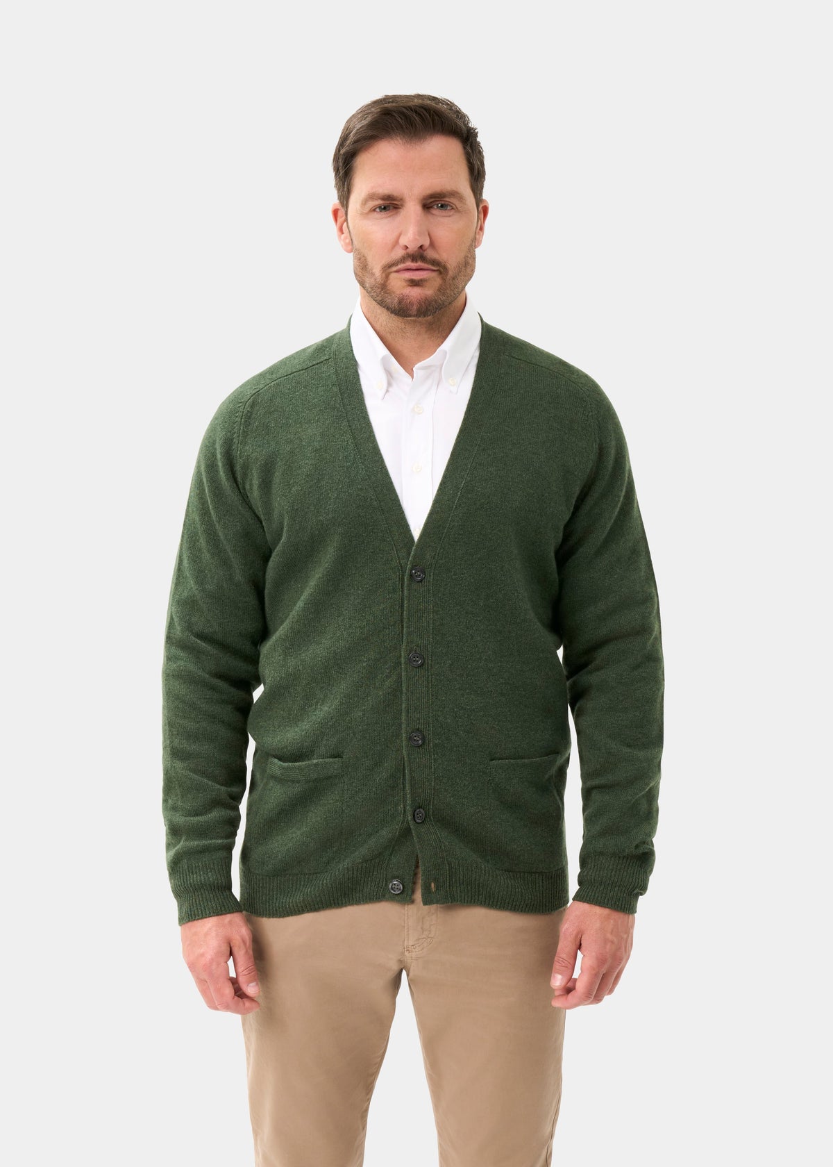 Man wears the Cornwall Lambswool V-Neck Cardigan in Rosemary over a white shirt and tan pants against a light background.