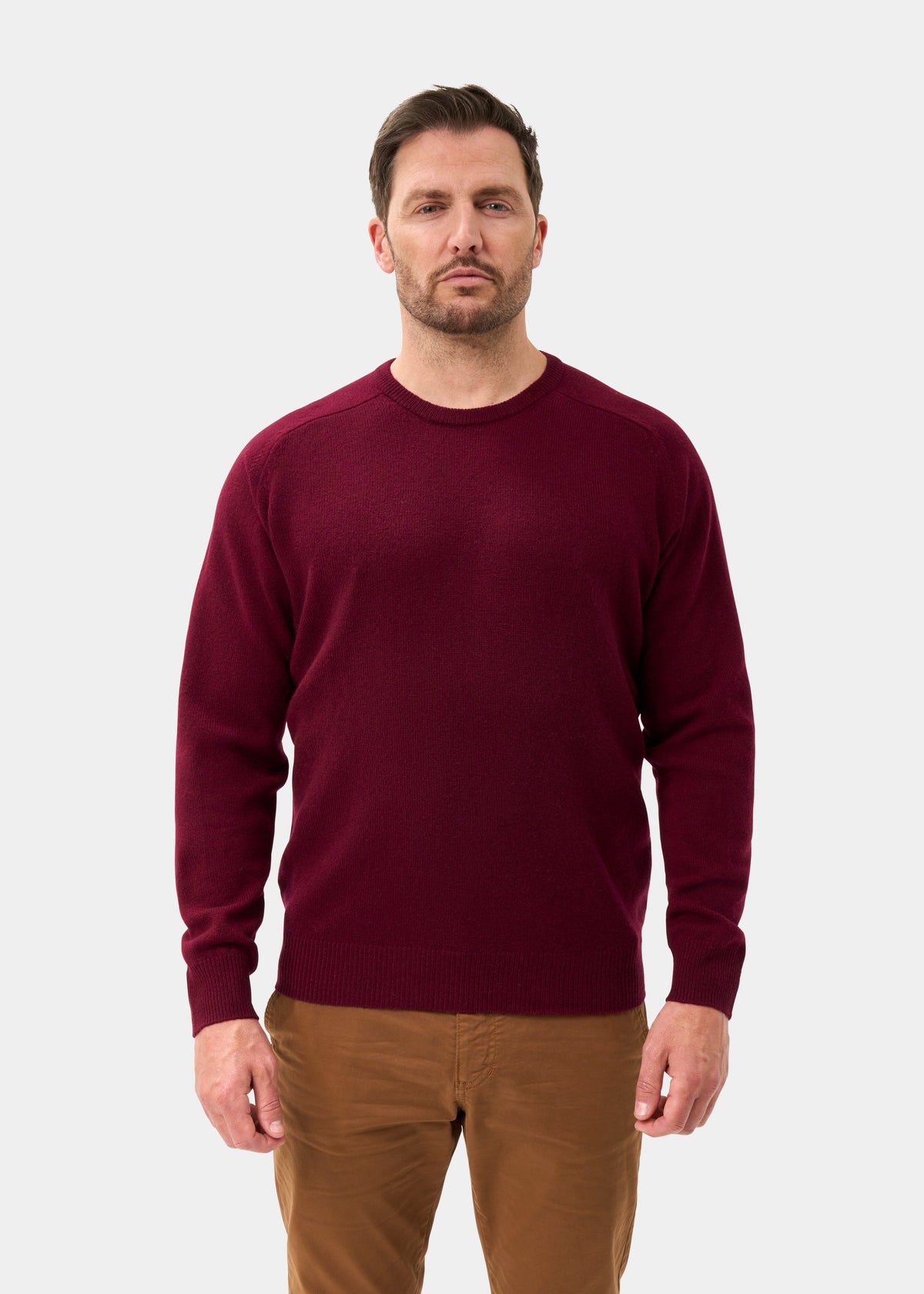 Man in Dorset Lambswool Crew Neck Jumper in Bordeaux and brown pants stands facing forward against a plain background.