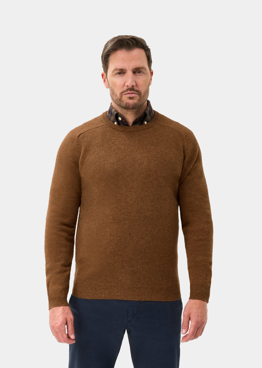 Man in Dorset Lambswool Crew Neck Jumper in Driftwood over plaid shirt, facing forward against white background.