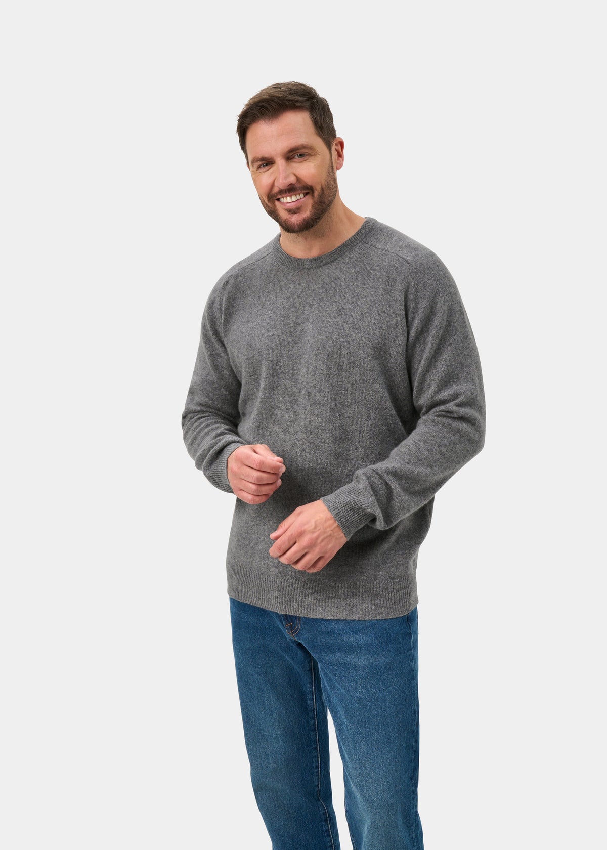 Man smiling in Dorset Lambswool Crew Neck Jumper In Grey Mix, blue jeans, against a plain white background.