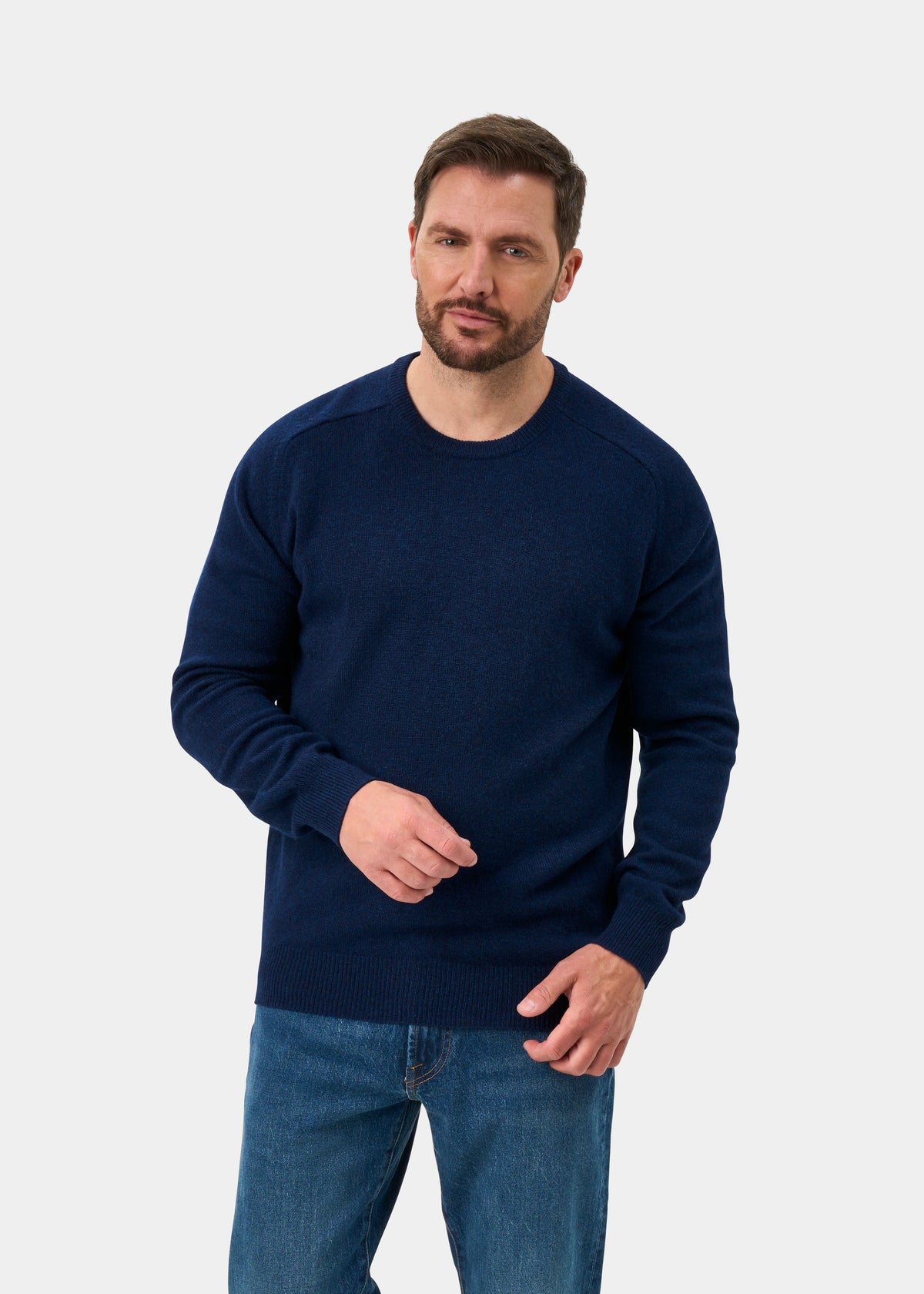 Man wears Dorset Lambswool Crew Neck Jumper in Indigo, classic fit, paired with jeans, on a white background.