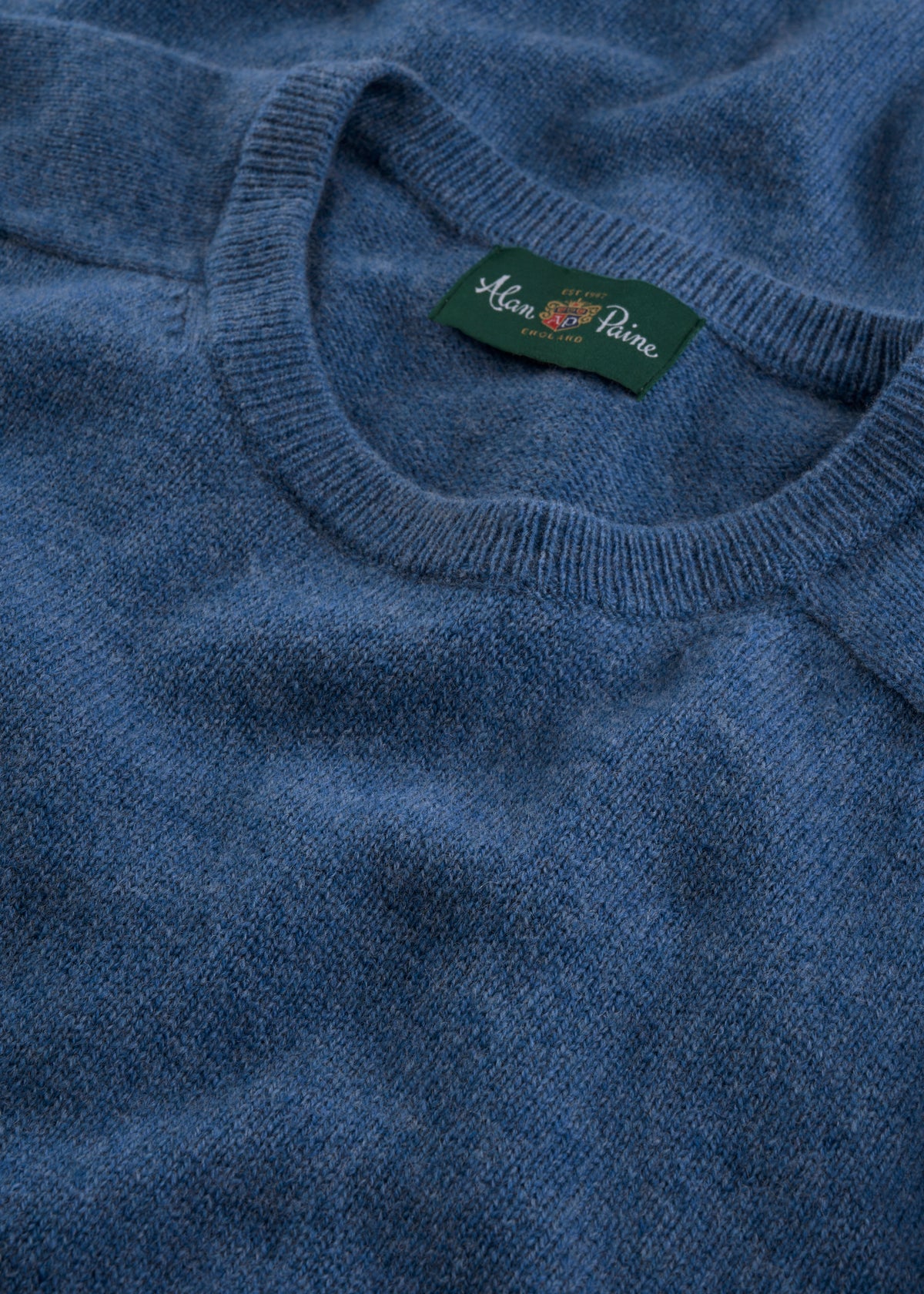 Close-up of the Lenzie Lambswool Crew Neck Jumper in Jeans with a green Alan Paine label at the neckline.