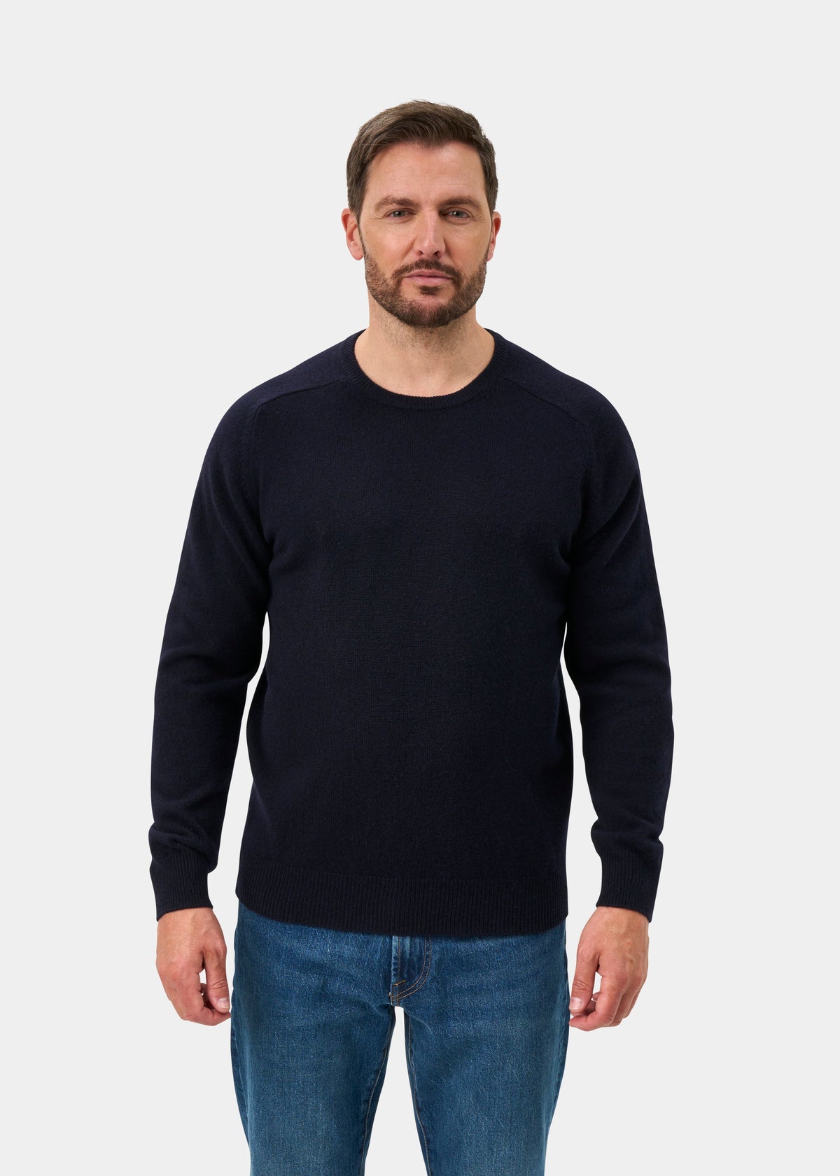 Man with short brown hair wears the Lenzie Lambswool Crew Neck Jumper in Navy, regular fit, and blue jeans.
