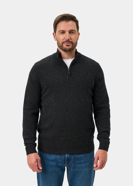 A man wears a Sutherland Lambswool Quarter Zip Jumper In Charcoal over a white t-shirt and blue jeans.