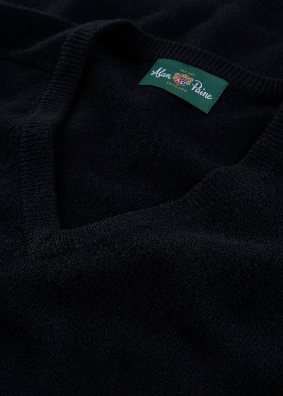 Close-up of the Hampshire Lambswool V-Neck Jumper in black, classic fit, with green Alan Paine collar label.