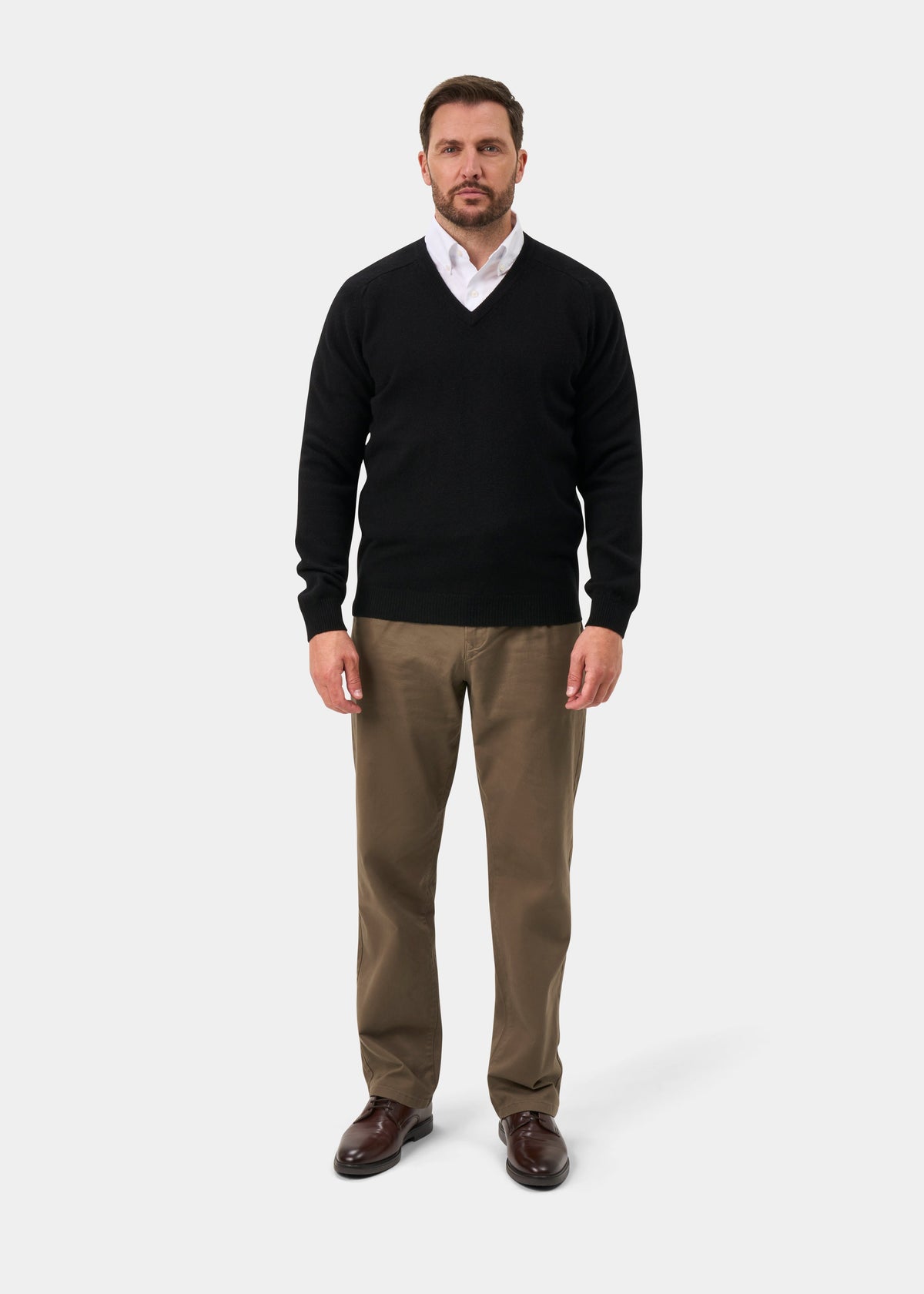 Man in Kilsyth Lambswool V-Neck Jumper in black over white shirt, khaki pants, and brown shoes on plain background.