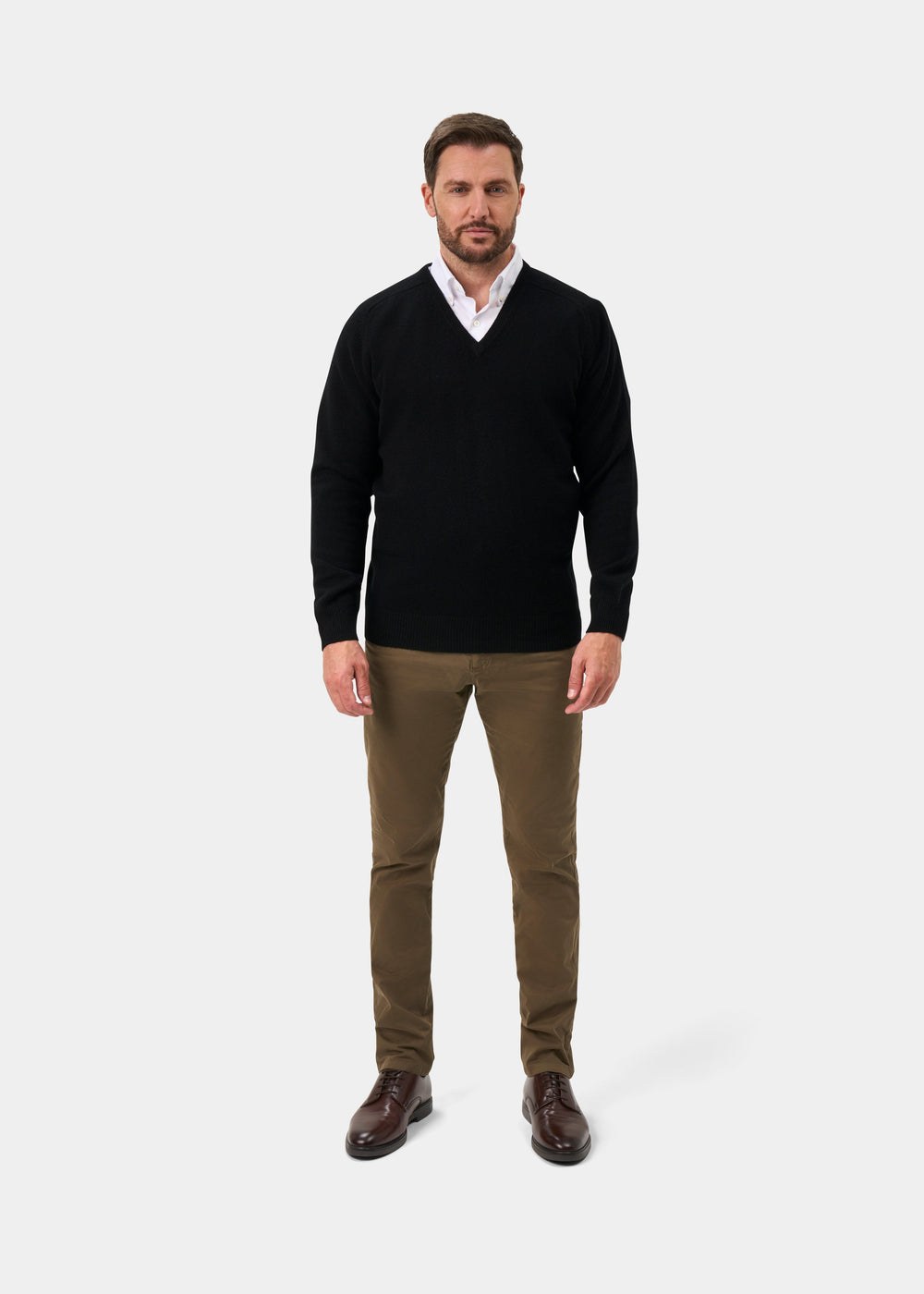 Man in Hampshire Lambswool V-Neck Jumper in black, white shirt, brown pants and shoes, against plain background.