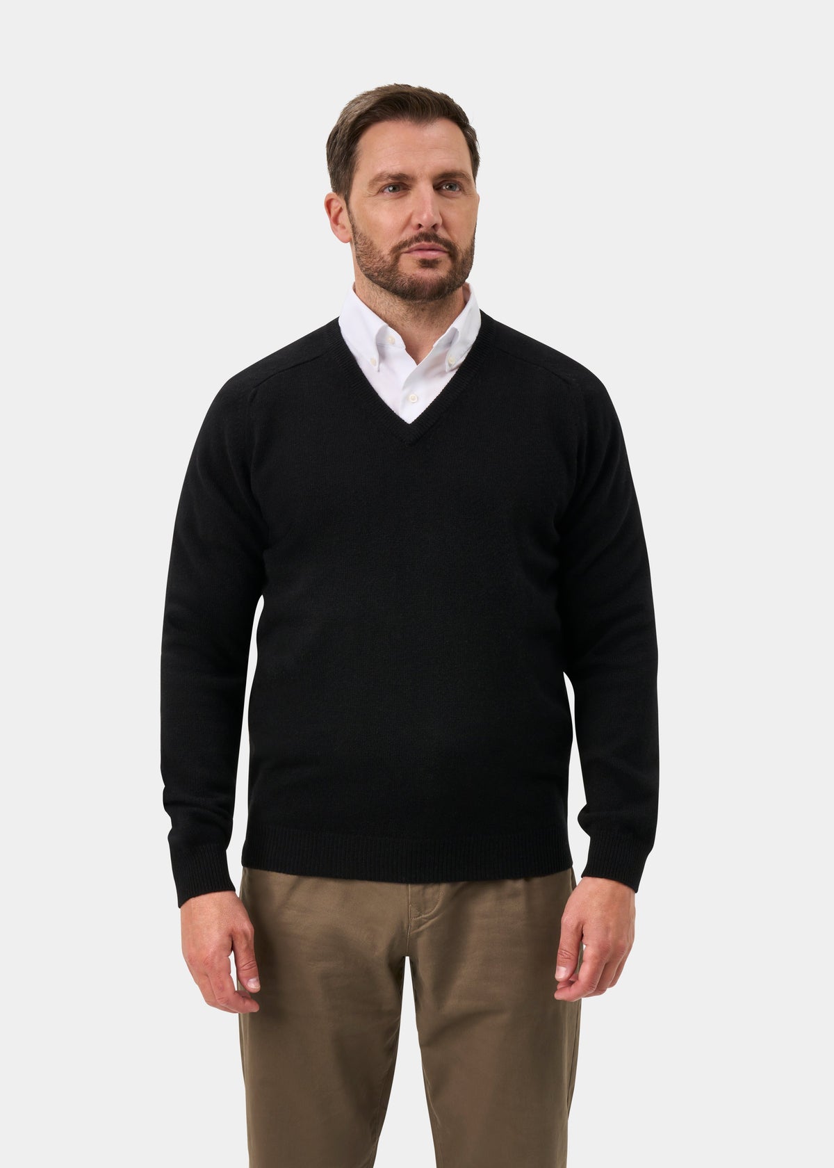 Man in Kilsyth Lambswool V-Neck Jumper (Black, Regular Fit), white shirt, tan pants; plain background.