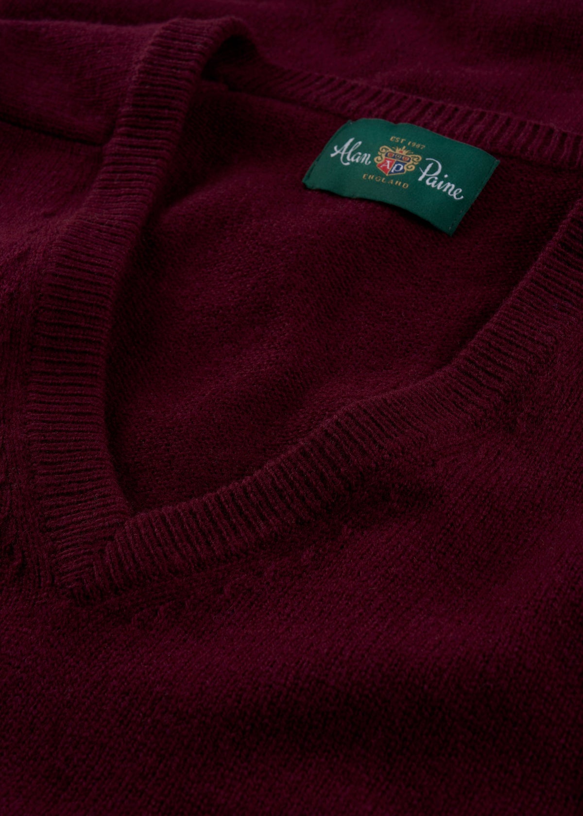 Close-up of the Hampshire Lambswool V-Neck Jumper in Bordeaux, classic fit, with a green Alan Paine England label.