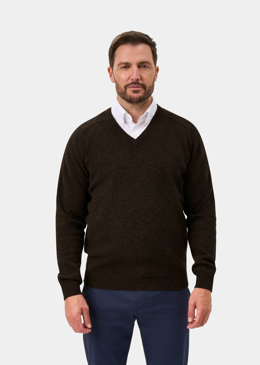 Man in Kilsyth Lambswool Vee Neck Jumper in Cocoa, over white shirt and blue pants, faces forward.