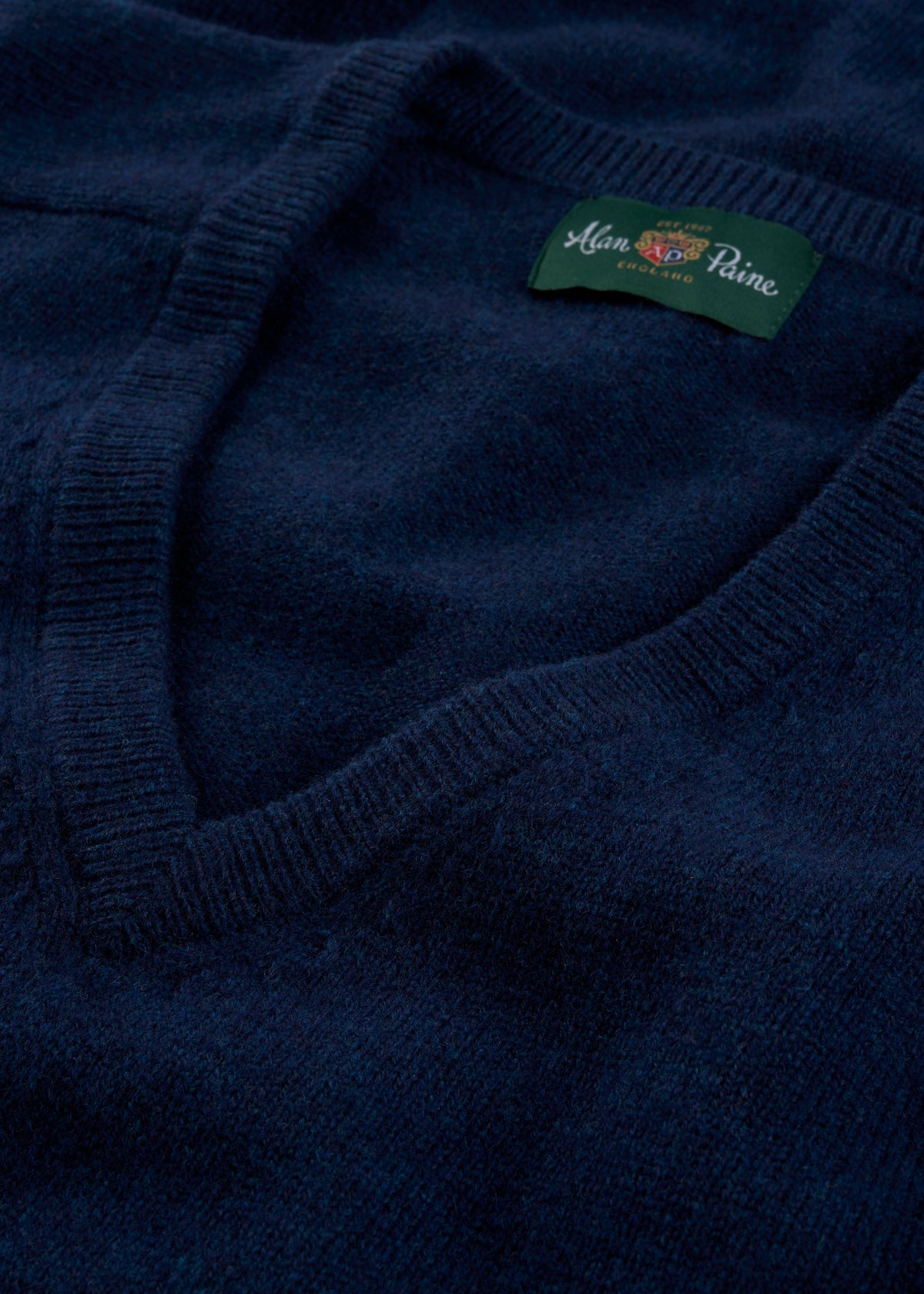 Close-up of the Hampshire Lambswool V-Neck Jumper in indigo, classic fit, with a green label at the collar.