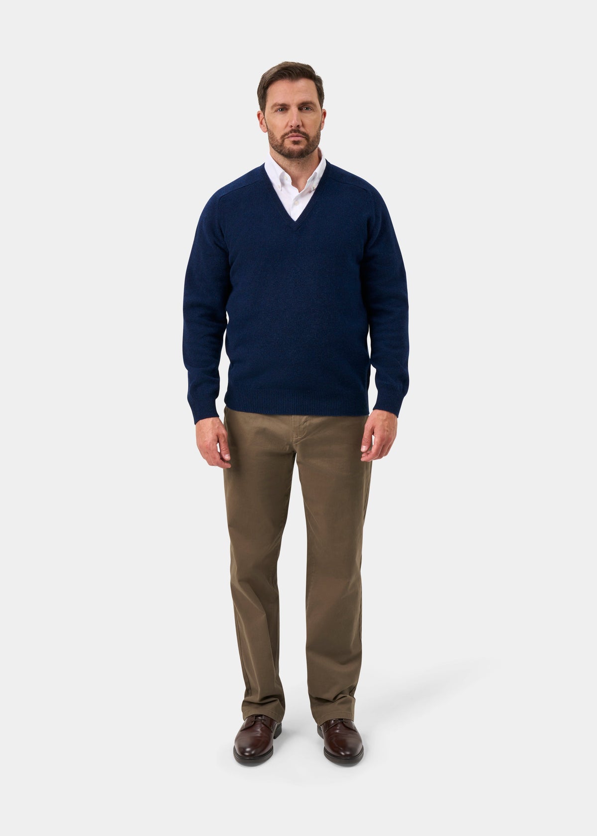 Man in Hampshire Lambswool V-Neck Jumper in Indigo, white shirt, khaki pants, and brown shoes on light background.