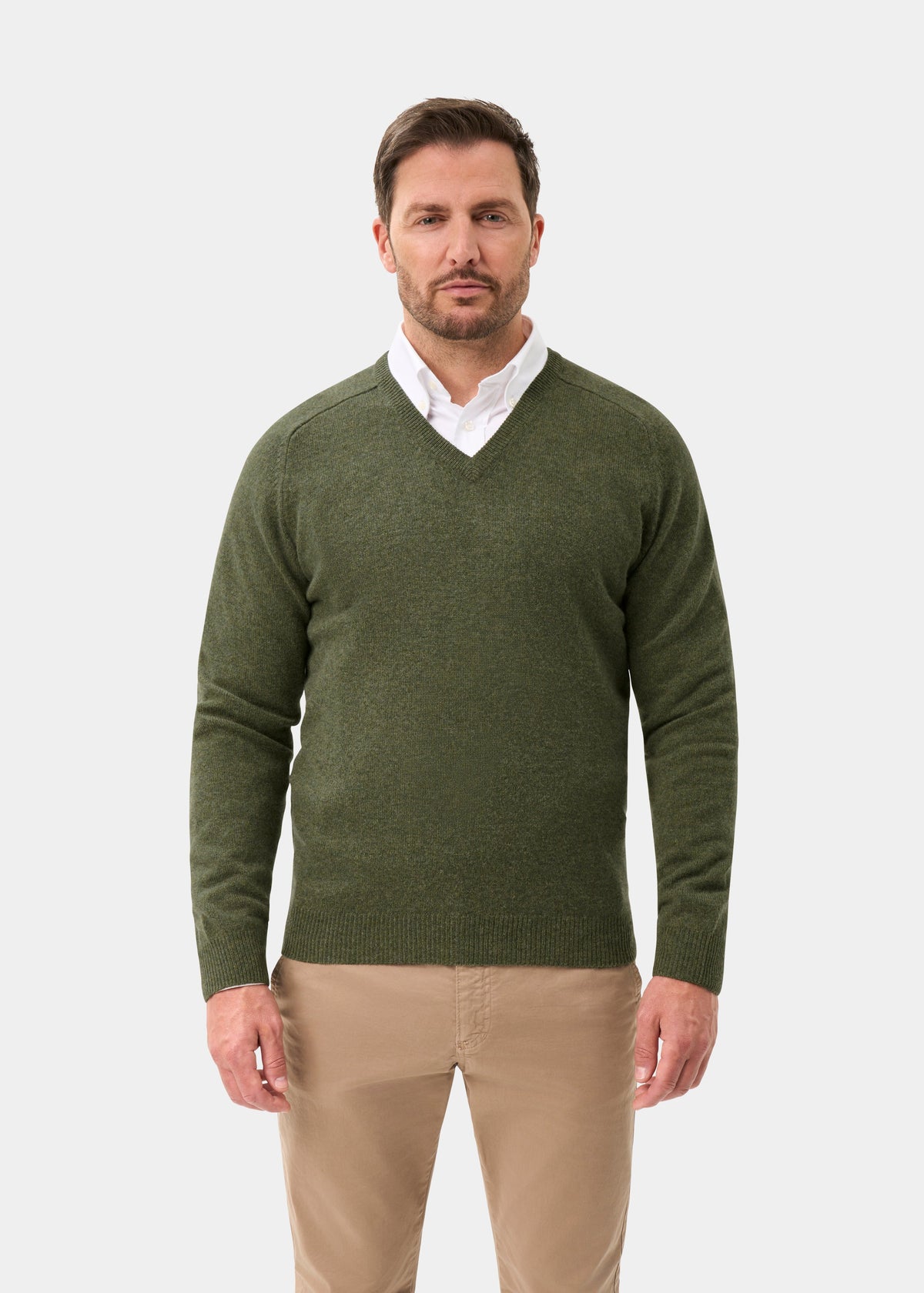 Man in Kilsyth Lambswool V-Neck Jumper in Landscape, white shirt, beige pants stands against plain background.