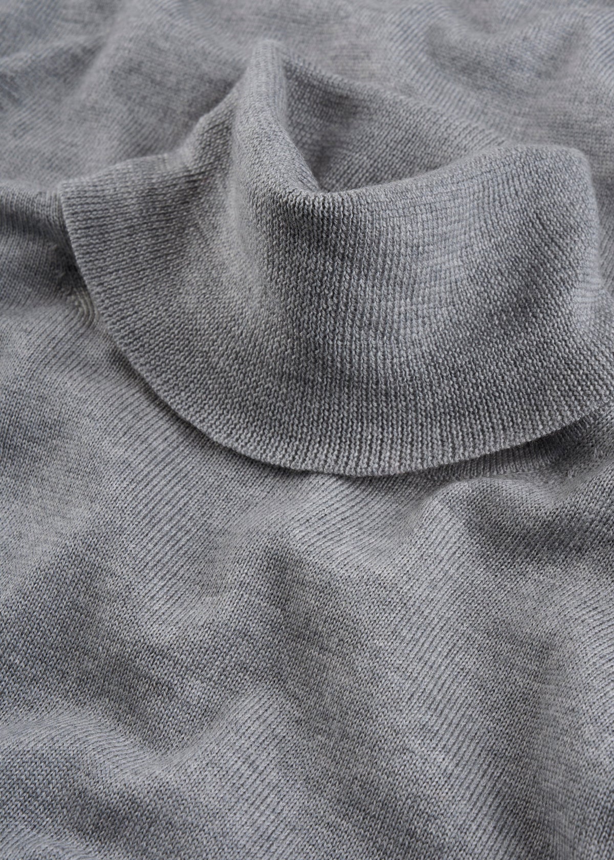 Close-up of the Linton Merino Wool Roll Neck Jumper in Light Grey Mix, showing off its soft knit and gentle folds.
