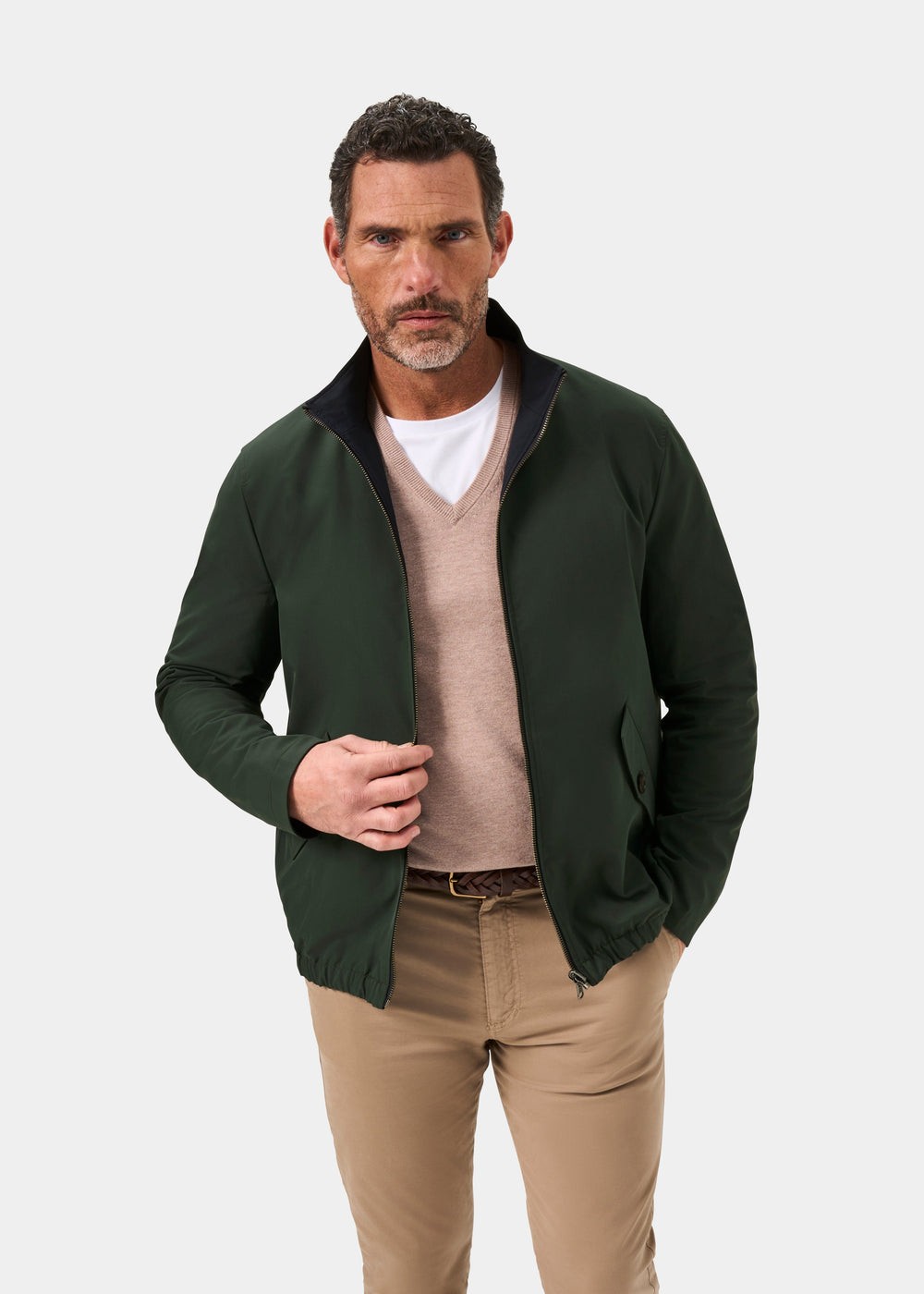 Man in a Lakeward green/navy reversible bomber jacket, beige sweater, and khaki pants stands by a plain white background.