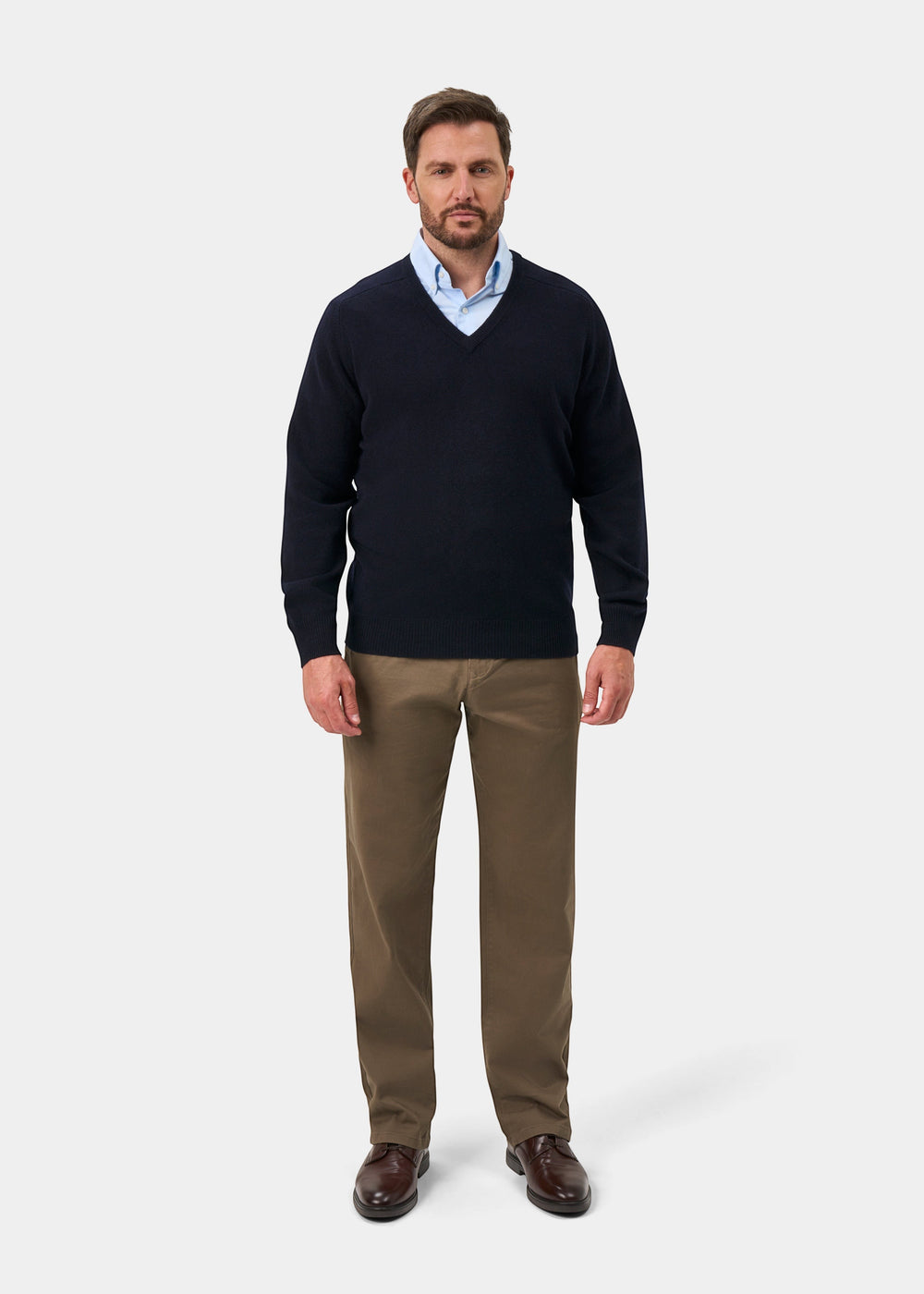 Man in Hampshire Lambswool V-Neck Jumper, navy, with a blue shirt, khaki pants, and brown shoes on white background.