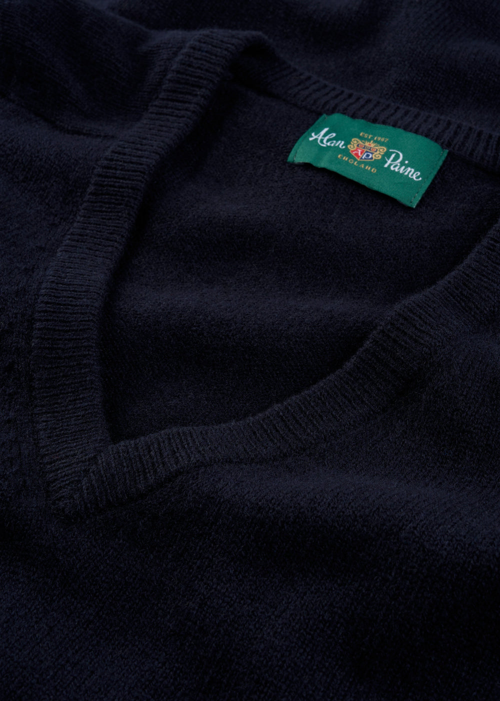 Close-up of Alan Paine’s Hampshire Lambswool V-Neck Jumper in navy, classic fit, featuring a green neck label.
