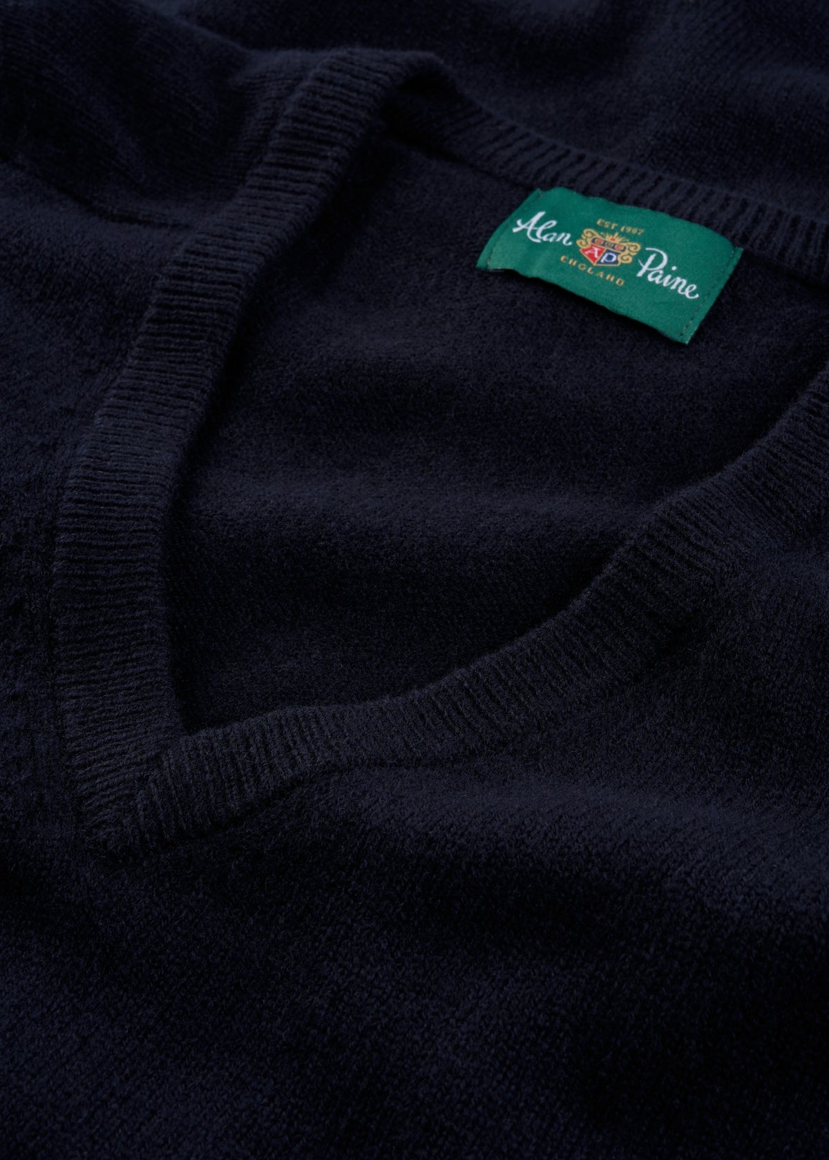 Close-up of Alan Paine’s Hampshire Lambswool V-Neck Jumper in navy, classic fit, featuring a green neck label.