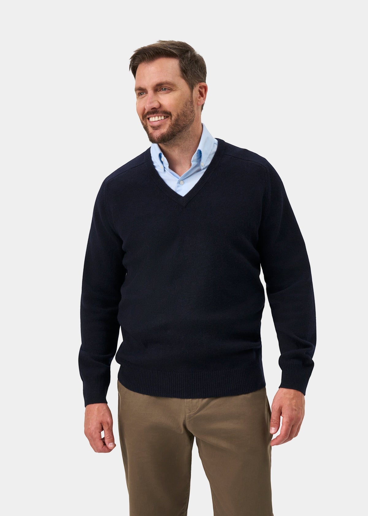 Man in Hampshire Lambswool V-Neck Jumper in Navy, light blue shirt, and khakis, smiling while standing.