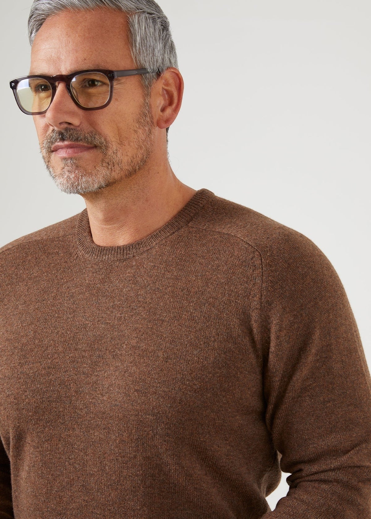 Man with gray hair wears Dorset Lambswool Crew Neck Jumper in Tobacco - Classic Fit, looking to the side.