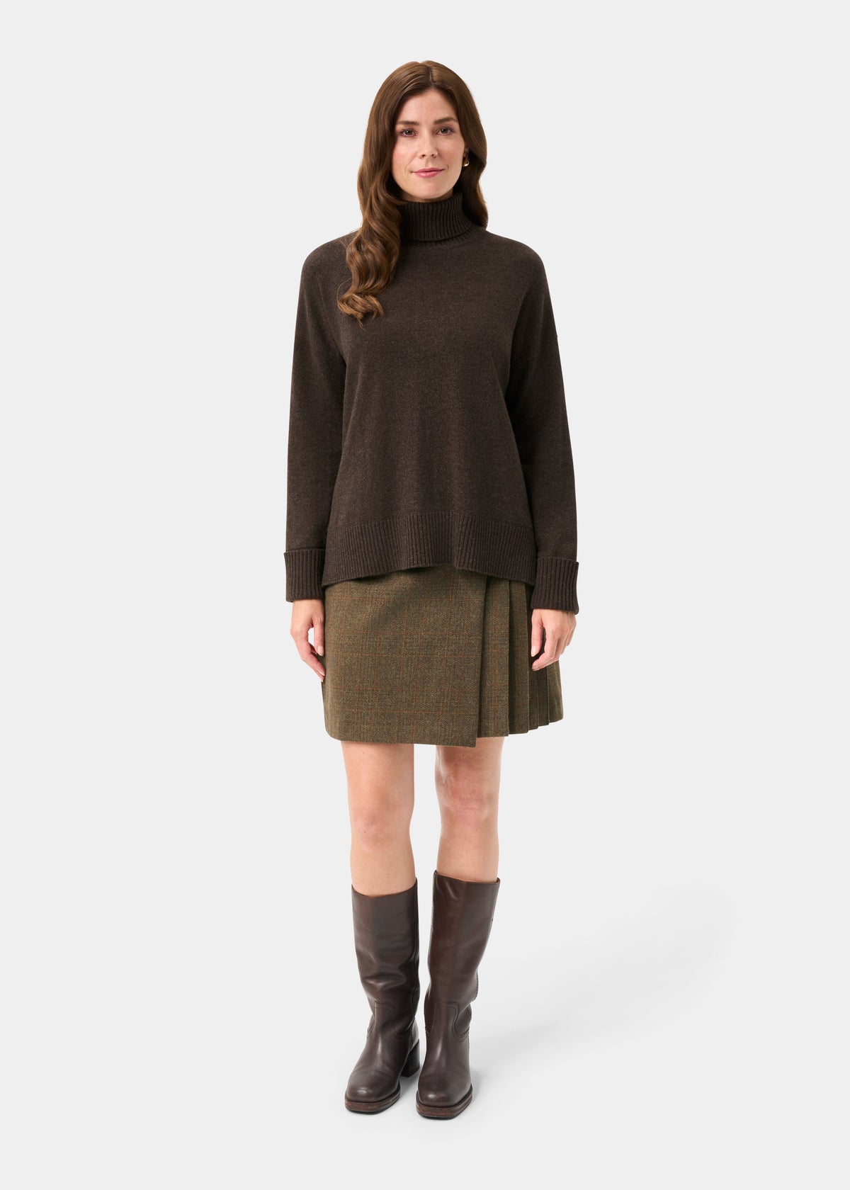 Woman wears Alexa Wool & Cashmere Roll Neck Jumper in Walnut, green skirt, and brown boots against white background.