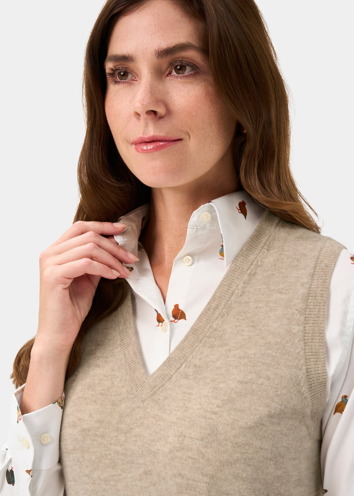 Woman in Erin Wool & Cashmere V-Neck Slipover in Porridge, over a white butterfly print shirt, looking aside.