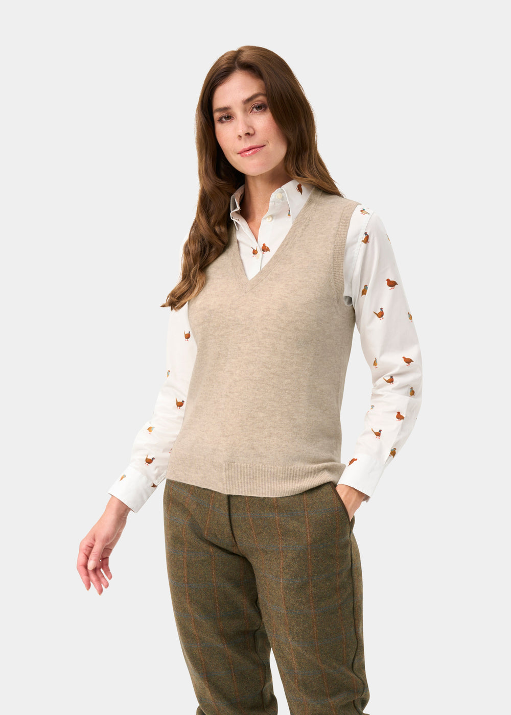 A woman wears the Erin Wool & Cashmere V-Neck Slipover in Porridge over a bird-print shirt and plaid trousers.