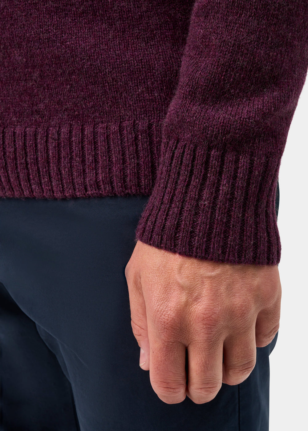 A person wears a Kinloch Supersoft Shetland Wool V-Neck Cardigan in Elderberry and navy pants, showing their hand.