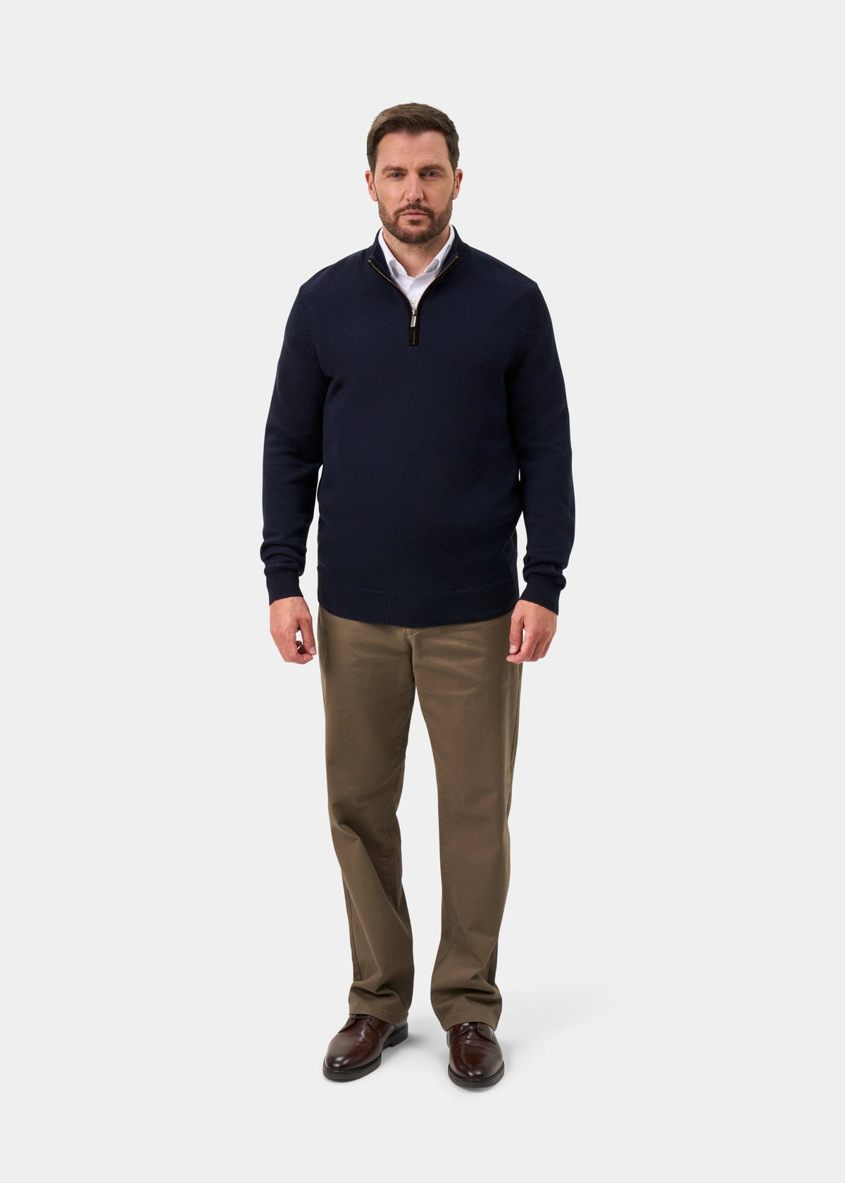 Man wears Kinmere Merino Wool Quarter Zip Jumper in dark navy, khaki pants, and brown shoes on a white background.