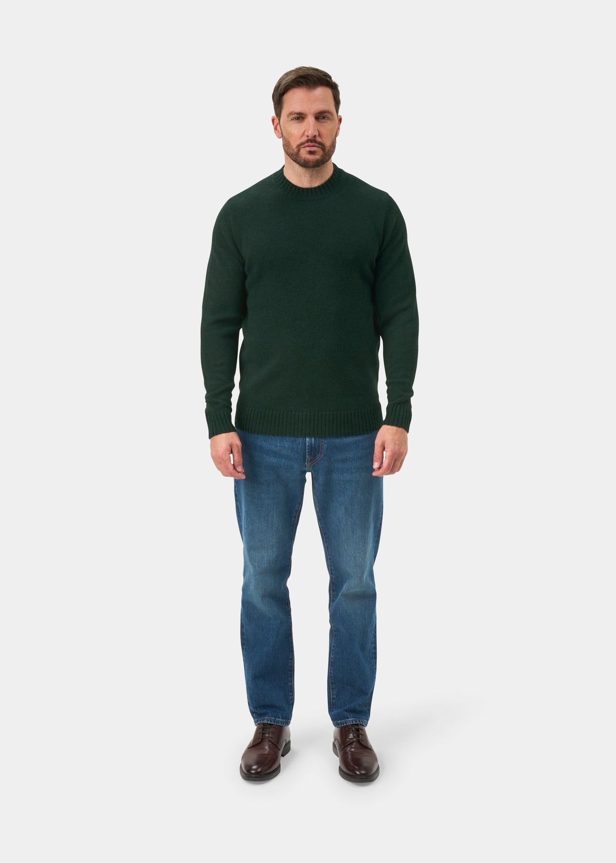 Man in a Kinnadie Supersoft Shetland Wool Crew Neck Jumper in Cossack, blue jeans, and brown shoes on white background.