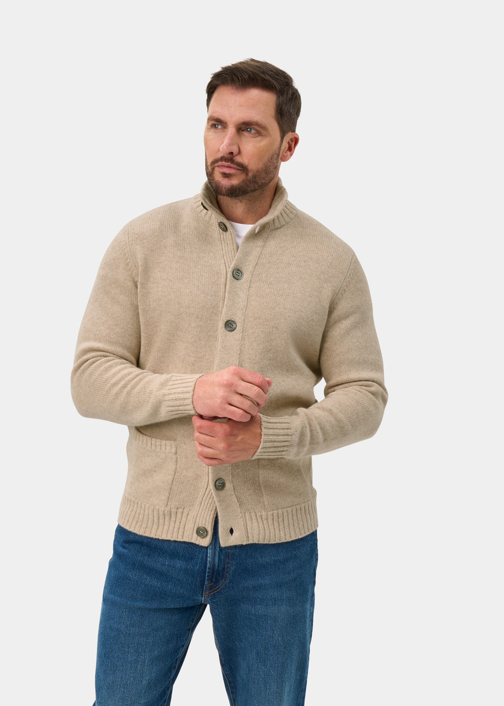 Man in Landford lambswool buttoned mock neck jumper in linen and jeans poses hands together against white background.