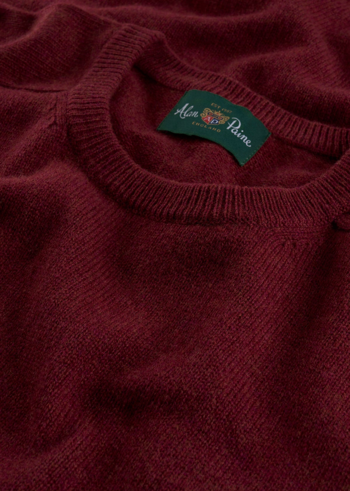 Close-up of the Lenzie Lambswool Crew Neck Jumper in garnet with the Alan Paine England label on the collar.