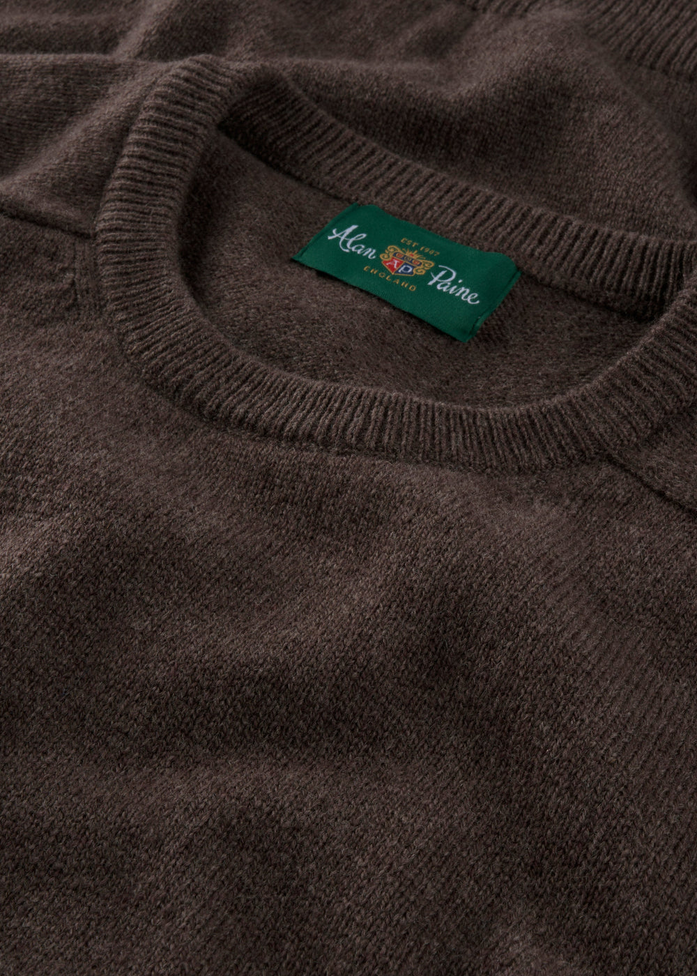 Close-up of the Lenzie Lambswool Crew Neck Jumper in Mocha with a green Alan Paine, England label and fine detailing.
